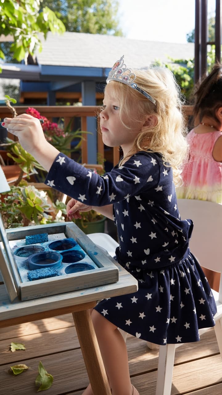 A preschooler in a star shirt paints at an outdoor easel